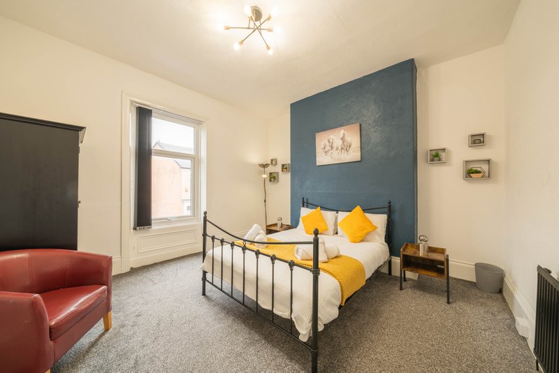 Bedroom with metal frame bed, yellow pillows, blue accent wall and red armchair