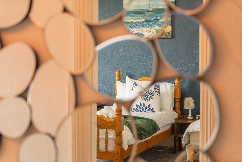 Bedroom with wooden bed, white bedding, blue accent wall, and coastal decor visible through doorway