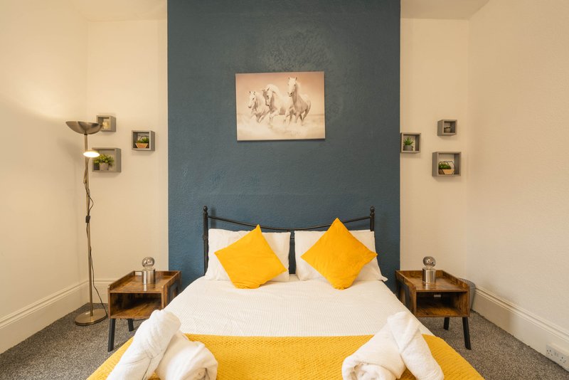 Modern bedroom with double bed, yellow pillows, blue feature wall and bedside tables
