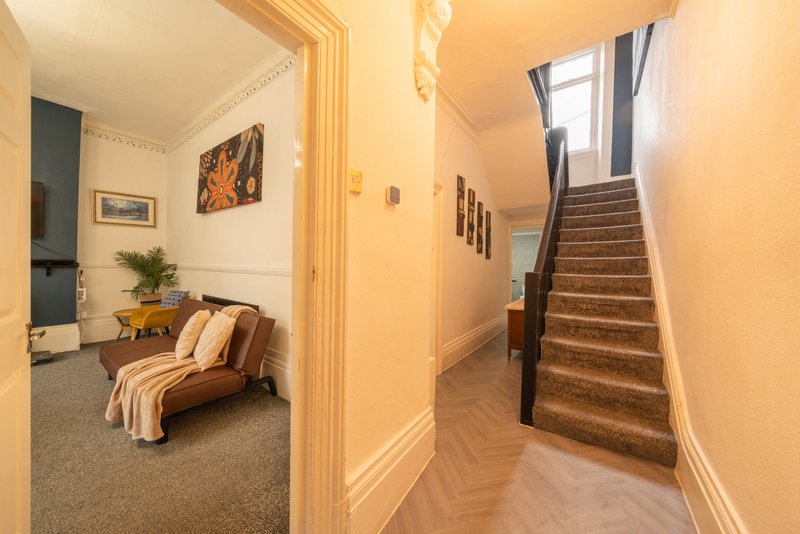 Hallway with wooden stairs and doorway to furnished sitting room with sofa