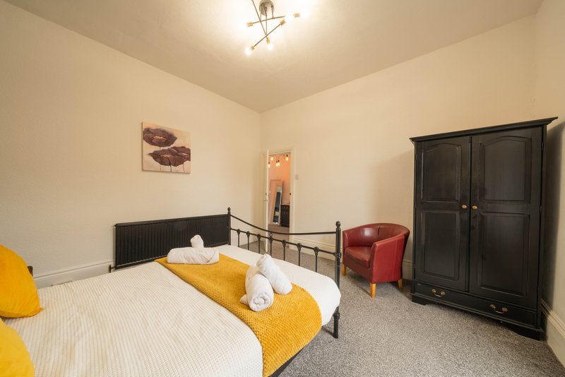 Bedroom with double bed, yellow bedding, black wardrobe, red armchair and wall art