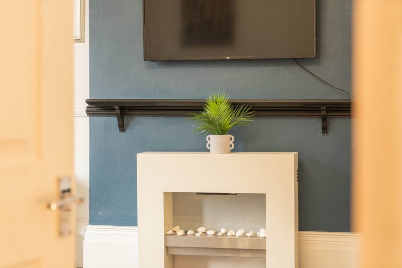 Living room with fireplace, wall-mounted TV, shelves and potted plant
