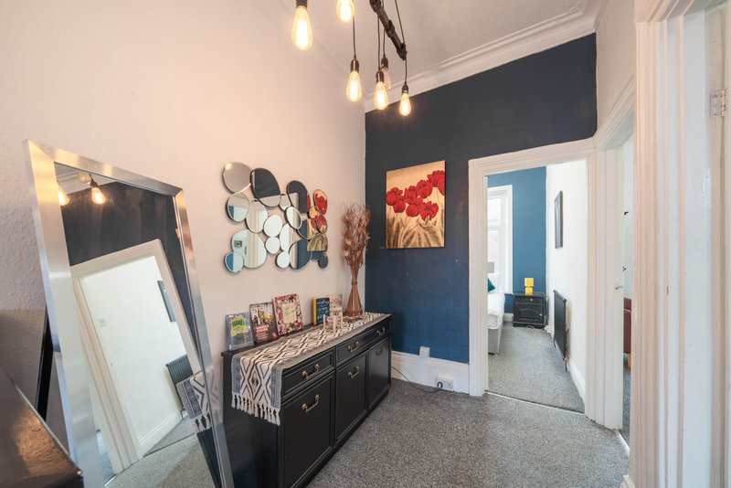 Hallway with dark blue accent wall, pendant lights, mirror, dresser and framed artwork