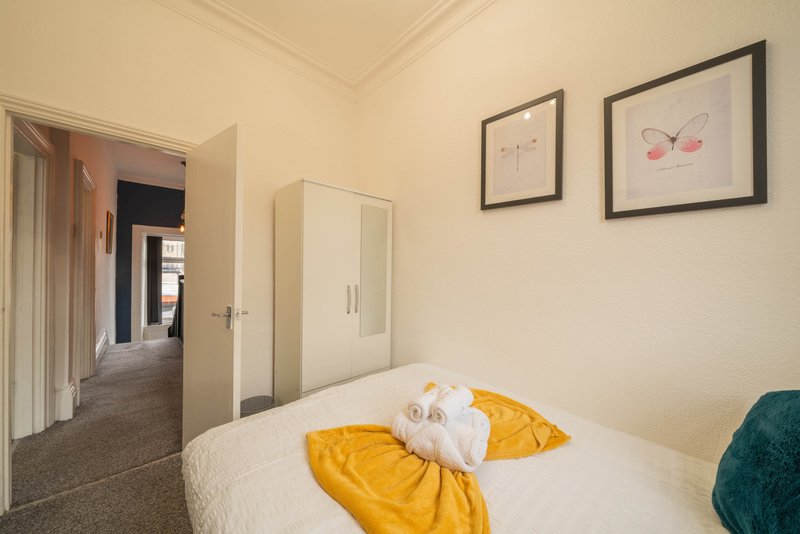 Bedroom with single bed, yellow pillows, wardrobe, framed artwork and open doorway