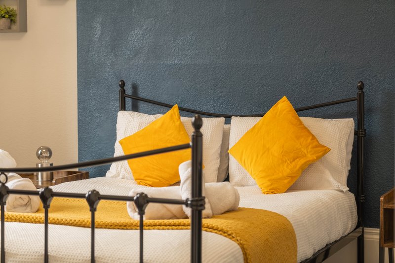 Bedroom with black metal bed frame, yellow pillows, white bedding and mustard throw