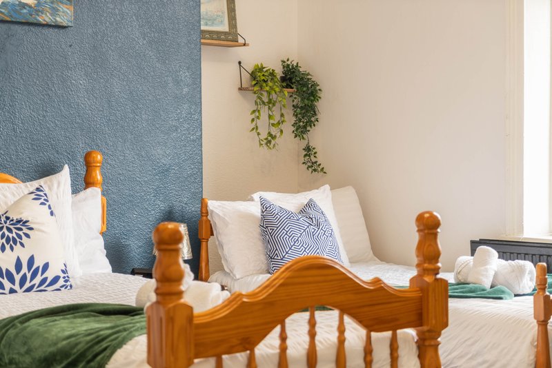 Bedroom with wooden bed frame, blue accent wall, white bedding and potted plant