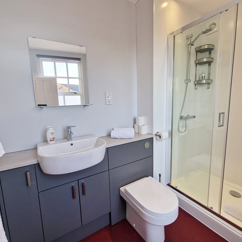 Modern bathroom with curved white sink, dark vanity, toilet, and walk-in shower enclosure