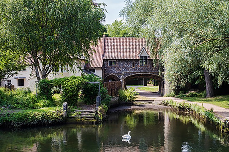 Rural brick house with red tile roof beside canal, trees and waterside setting