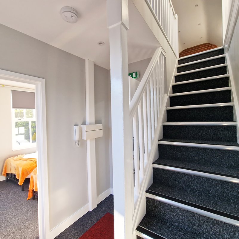 Bright stairwell with black-carpeted stairs, white railings, and cream walls leading upstairs