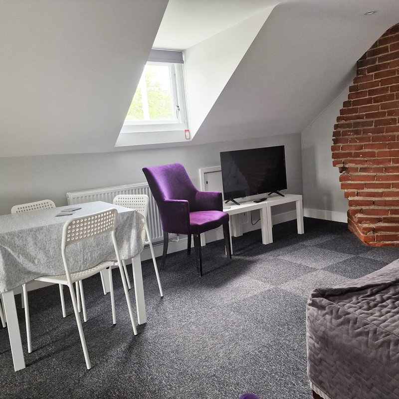Attic studio with skylight, dining table, purple chair, TV, and exposed brick wall