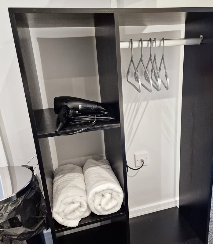 Open shelving unit with rolled towels, hair dryer, and hanging wire hangers