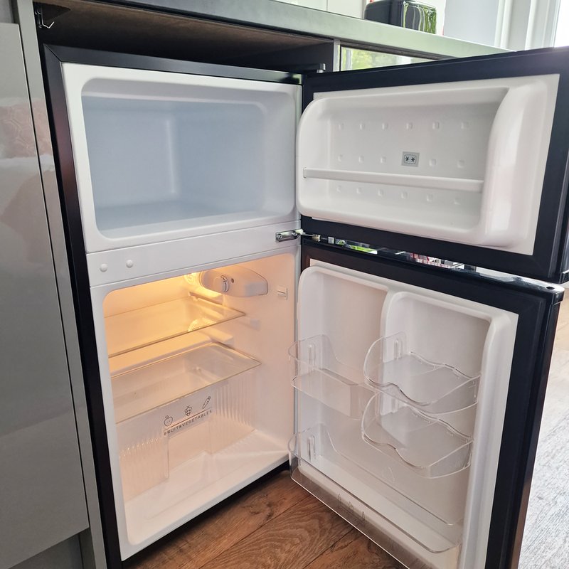 Open black and white compact refrigerator with empty shelves and freezer compartment