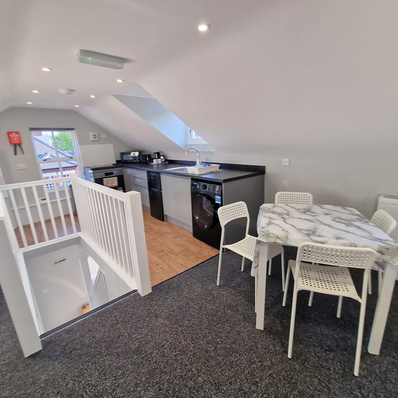 Attic room with kitchenette, white crib, dining table, chairs and skylight window