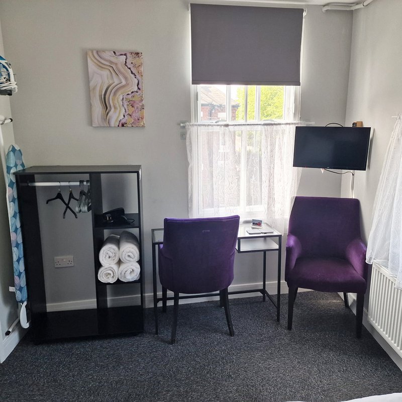 Modern bedroom corner with purple chairs, TV, storage unit and window with blinds