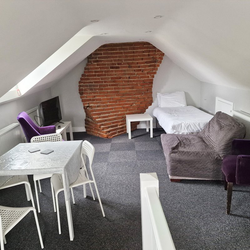 Attic bedroom with exposed brick wall, bed, dining table, chairs and purple accent furniture