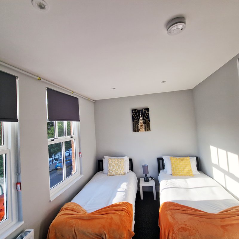 Twin bedroom with orange bedding, yellow cushions, windows and wall art