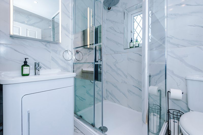 Bathroom 1: Modern bathroom with marble tiles, walk-in shower, white vanity and mirror