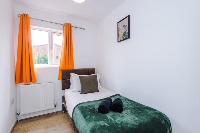 Compact bedroom with single bed, green bedcover, orange curtains and window view