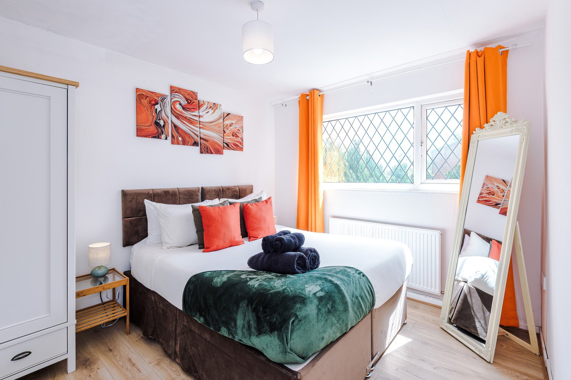 Bedroom 2: King Size Zip Link Bed which can be split into 2x single beds - Bright bedroom with double bed, orange curtains, wall art, and leaning mirror