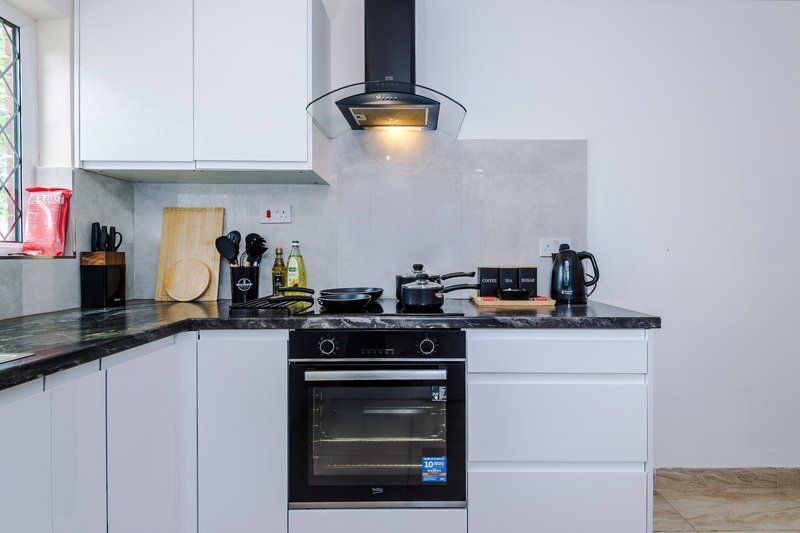 Modern white kitchen with black countertop, gas stove, hood vent, and cooking utensils
