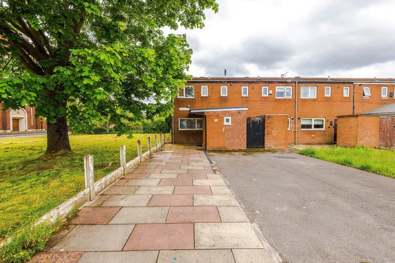 Brick residential building exterior with paved pathway, green lawn, and mature tree