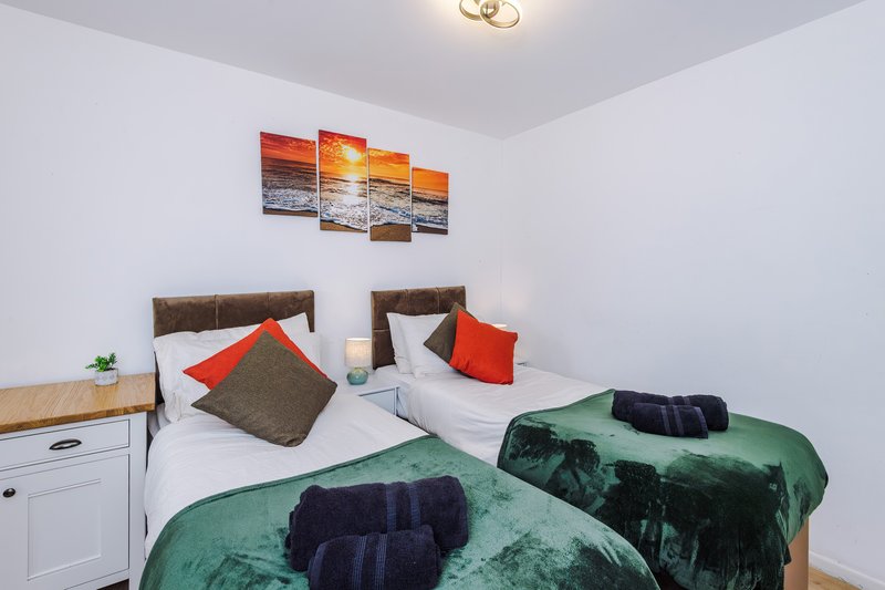 Twin bedroom with white walls, two beds with green throws, and sunset artwork above headboards