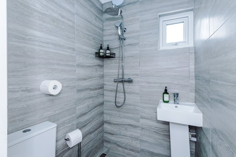 Bathroom 2: Modern bathroom with grey tile walls, walk-in shower, pedestal sink, toilet and window