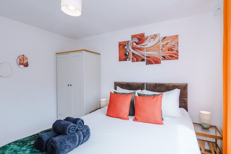 Bedroom 2: King Size Zip Link Bed which can be split into 2x single beds - Bright bedroom with double bed, orange curtains, wall art, and leaning mirror