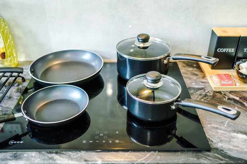 Kitchen stovetop with induction hob, pans, and cooking utensils on counter