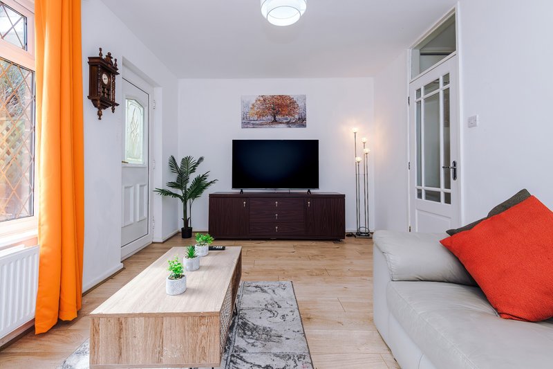 Modern living room with TV, wooden furniture, orange curtains and red cushions