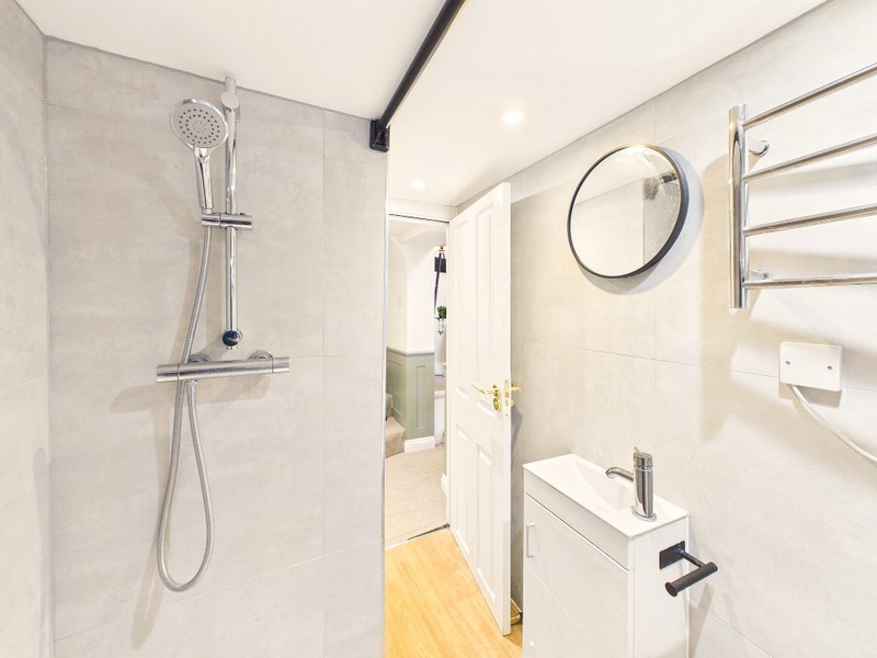 Modern bathroom with rainfall showerhead, white vanity sink, heated towel rail and circular mirror