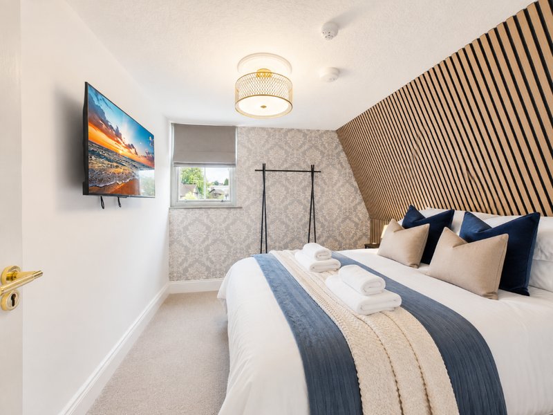 Modern bedroom with double bed, TV on wall, wooden accent wall and ceiling light