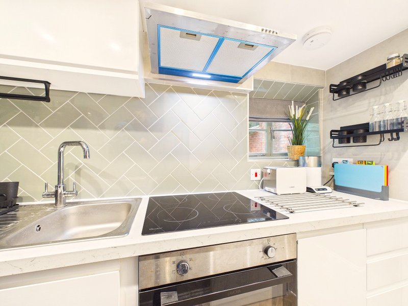 Modern white kitchen with herringbone tile splashback, induction hob, sink and stainless steel appliances