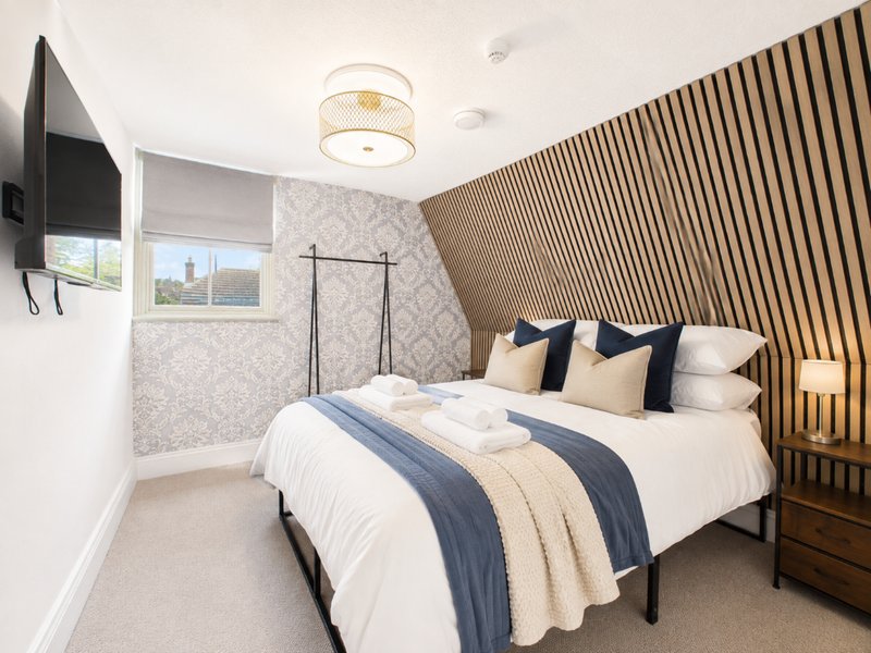Modern bedroom with double bed, wooden slat headboard, wall-mounted TV and ensuite bathroom