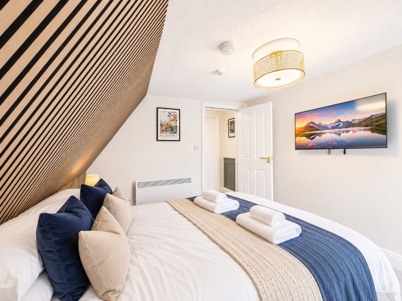 Modern bedroom with double bed, blue cushions, white bedding, and landscape artwork on wall