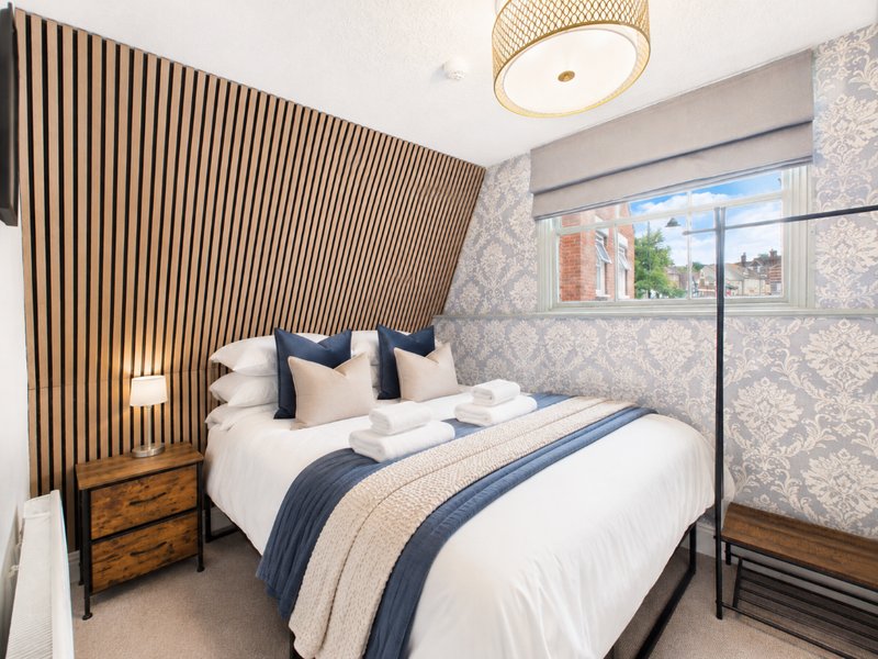 Modern bedroom with double bed, blue bedding, wooden slat wall feature, and city views from window