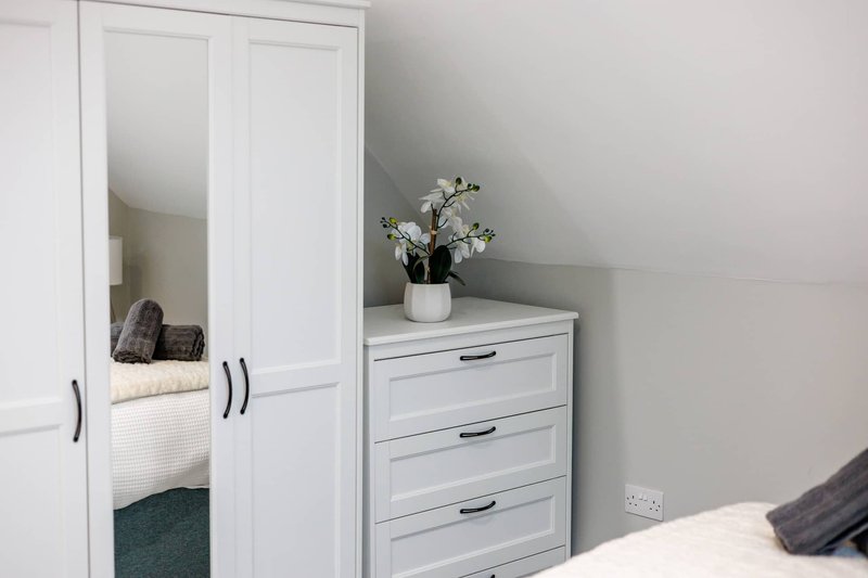 Modern bedroom with white wardrobe, chest of drawers, flowers in vase, and bed