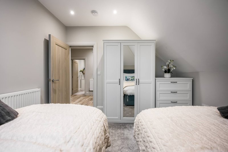 Bright bedroom with two single beds, built-in wardrobe, chest of drawers and ensuite door