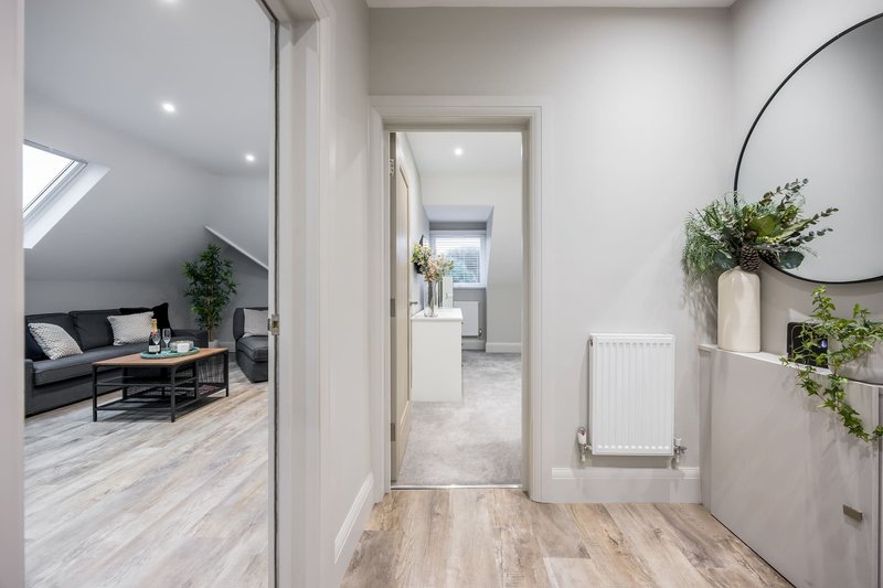 Modern hallway with wooden flooring, white walls, round mirror and potted plants
