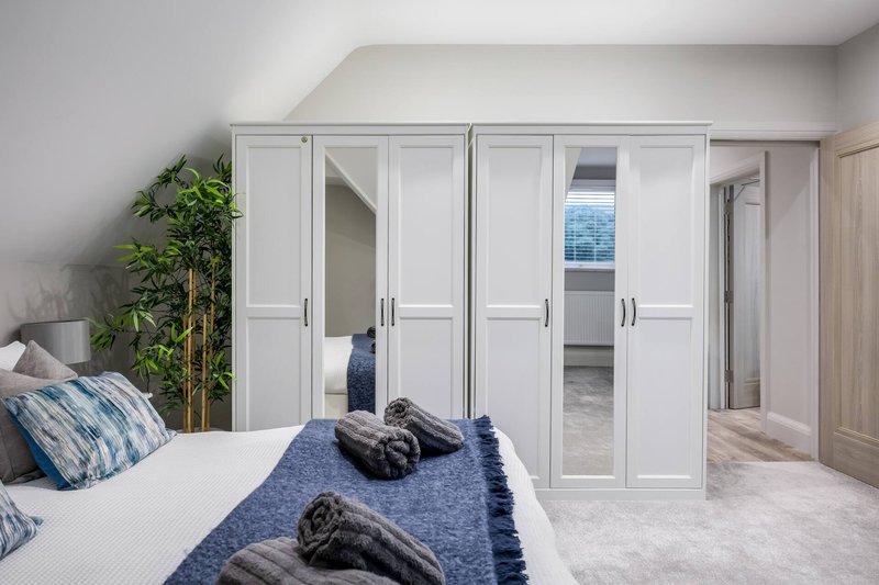 Bright modern bedroom with double bed, blue bedding, white fitted wardrobes and potted plant