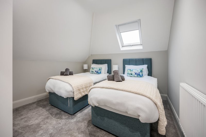 Twin bedroom with two beds, blue headboards, cream bedding, skylight window and radiator