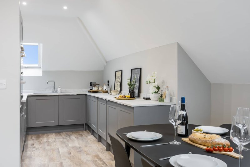 Modern kitchen with gray cabinetry, white countertop, dining table with place settings and wine bottle