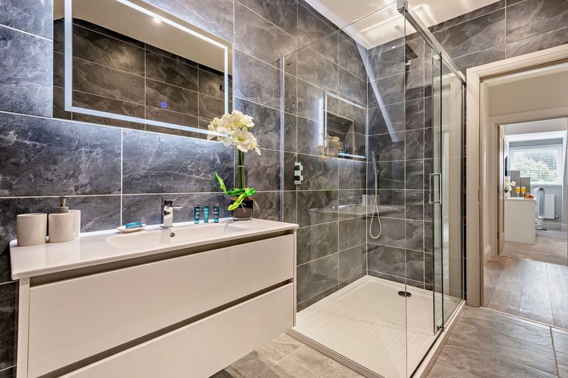 Modern bathroom with grey tile walls, white vanity, mirror and enclosed shower enclosure