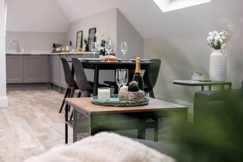 Modern open-plan kitchen and dining area with dining table, chairs, and champagne bottle on counter