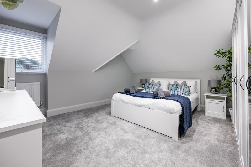 Modern attic bedroom with white bed, grey carpet, sloped ceiling and potted plants