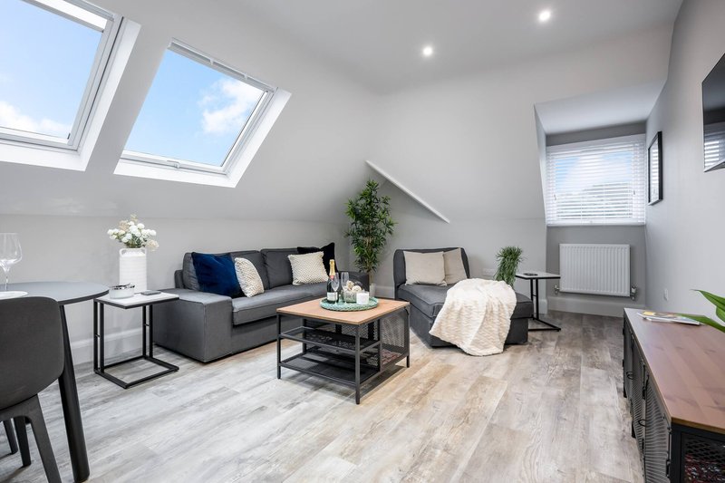 Bright attic living room with grey sofa, wooden coffee table, skylight windows and potted plants