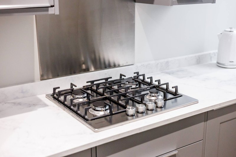 Modern kitchen with gas cooktop on white marble countertop and stainless steel backsplash