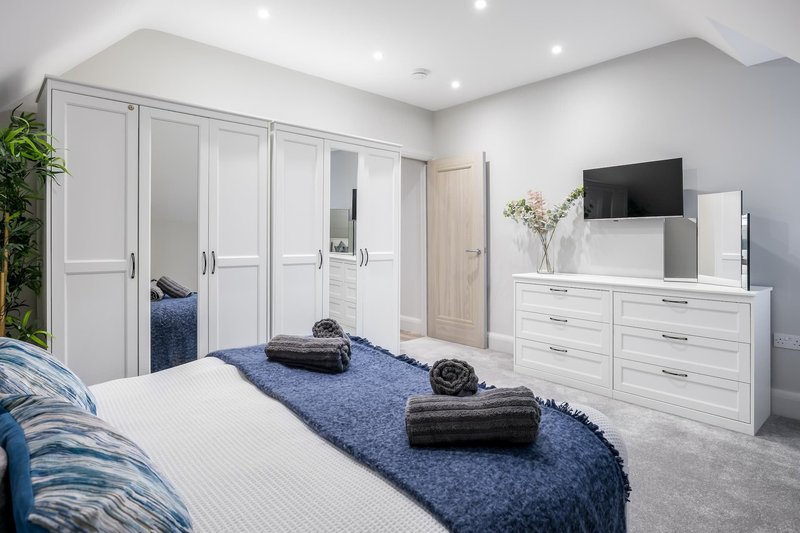 Modern bedroom with white wardrobe, double bed, dresser with TV, and blue accent rug