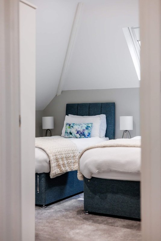 Attic bedroom with twin beds, dark upholstered headboard, white bedding, sloped ceiling and skylights