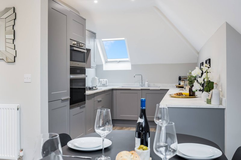 Modern kitchen with gray cabinetry, dining table set with wine bottle and glasses, skylight window